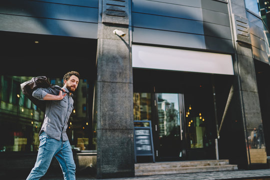 Portrait Of Bearded Hipster Guy Holding Sport Bag On Back And Strolling Near Shopping Center In Modern City.Confident Young Man Dressed In Casual Wear Walking In Urban Setting And Going To Gym