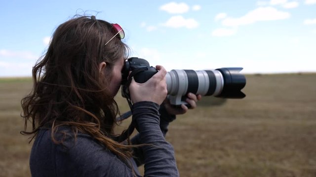 A female photographer uses a professional camera and telephoto lens to capture the landscape. She stands in a field and snapping photos in slow motion