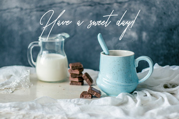 Pastel blue coffee mug, bottle of milk and chocolate on rustic table with greeting quote
