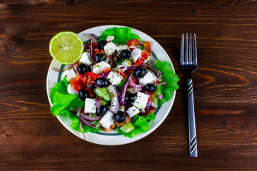 plate of tasty healthy greek salad on a blrown wooden table , national dish of Greece on a beautiful background , greek's kitchen with spices , fork and lemon
