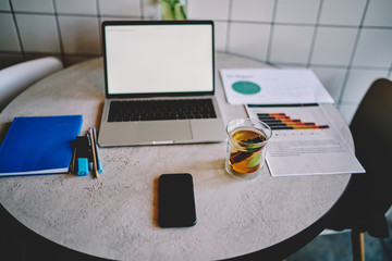Modern laptop computer with blank screen area for your internet content staying on table with office equipment for work.Desktop with netbook and paper documents with diagrams in workspace