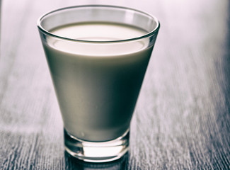 Milk in a glass cup on a wooden background. Photographed close-up in a low key.