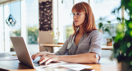 Side view of clever female it professional updating information for database of cafetria working...