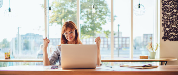 Overjoyed young woman raising hands celebrating achievement victory in online games on laptop...