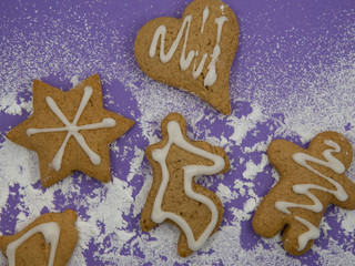 Gingerbread cookies with sugar icing on powdered sugar in front of violet background