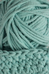 Knitting and hand crochet concept. A fragment of a knitted product and a ball of cord close up. Tiffany color yarn background.