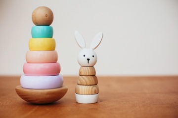 Stylish wooden toys for child on wooden table. Modern colorful wooden pyramid with rings and simple bunny. Eco friendly, plastic free educational toys for toddler