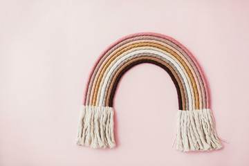 Stylish macrame rainbow decoration on pink background. Modern boho  rope rainbow for baby room or simple stylish girl room. Wall hanging macrame decor