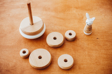 Stylish wooden toys for child on wooden table. Modern simple wooden pyramid with disassembled rings...
