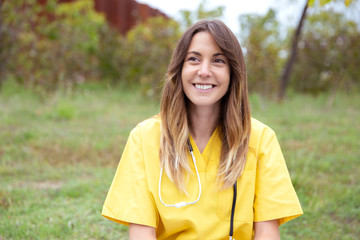 Retrato de enfermera joven sentada en parque vestida con uniforme amarillo