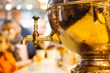 Samovar - a Russian kettle for boiling water of gold color on a background with people.