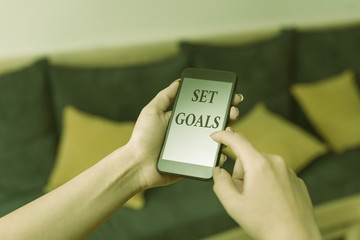 Word writing text Set Goals. Business photo showcasing Defining or achieving something in the future based on plan woman using smartphone office supplies technological devices inside home