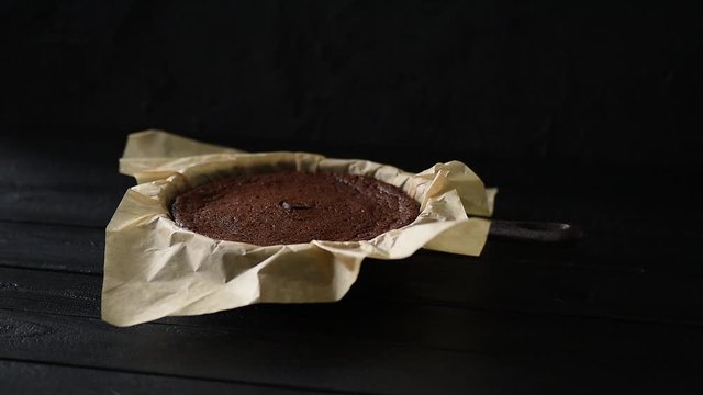 Homemade pastry concept. Fresh chocolate cake kladdkaka quickly collapsing after baking in cast iron pan on black background low key copy space
