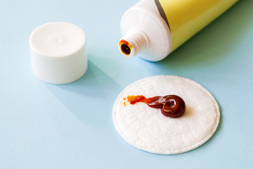 Some iodine ointment on a cotton pad near an open tube over a blue background. The salve is used for small wounds and for skin disinfection before and after surgery.
