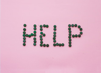  word "help" made from green pills on a white background