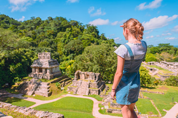 Young woman walking through the ancient Mayan ruins of Palenque, watching the pyramids on a sunny day.