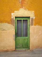 Green entrance door with glass at home of yellow colored old walls