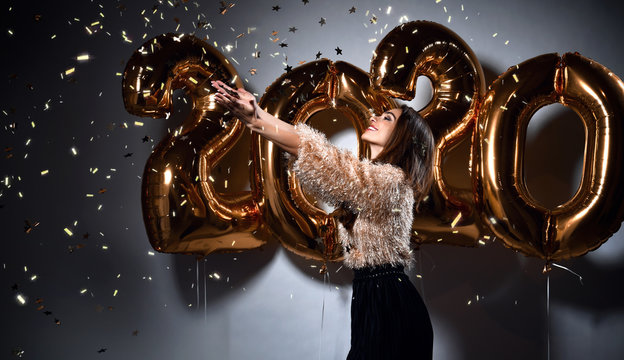 Beautiful woman celebrating New Year with gold 2020 balloons. Happy gorgeous girl in stylish sexy party dress