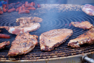 Ribs, pieces of meat and sausages lie in smoke on a brazier fire at a red pepper festival in a small town
