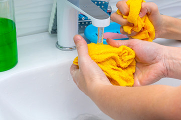 Cloth in hands under a stream of water. Hands of a woman and a child. Yellow cloth and hands under running water. Concept: hygiene and cleaning, education, maintenance of cleanliness.