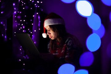 young girl with a laptop in the New Year sits alone at home and is sad in Christmas clothes, a woman is online at Christmas