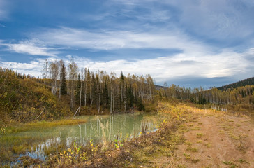 autumn landscape in the mountains, a small lake wild impassable natural places, white clouds in the blue sky