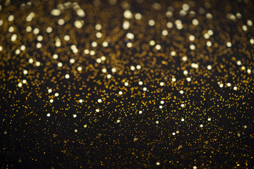 Beautiful Christmas light background. Abstract glitter bokeh and scattered sparkles in gold, on black
