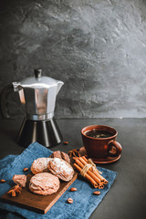 Chocolate cookies, cup with coffee, moka pot, cinnamon sticks, star anise on blue napkin, dark background with copy space