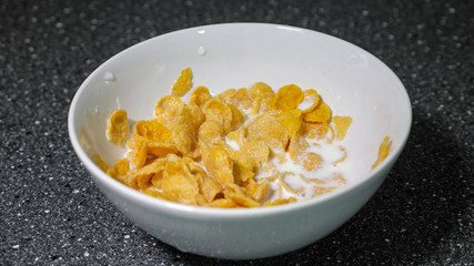 Preparing fast breakfast with cereal. dry cornflakes and milk in bowl with spoon.