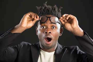 handsome african man in a suit on a black background with glasses with a surprised face