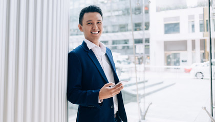Fototapeta premium Successful young modern Asian businessman using smartphone in downtown