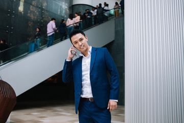 Young Asian businessman talking on smartphone and looking at camera