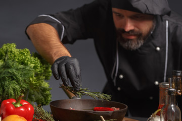 Male chef in a black uniform slices a knife with pork meat on a wooden board. Close-up. Cooking process