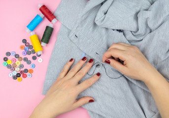 a girl with a needle in her hands sews a button to a shirt.