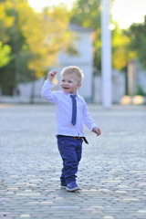 Naklejka premium Young little boy in suit with smile walks in the street