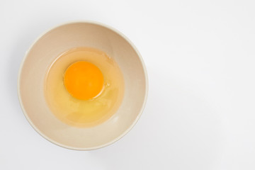 Broken egg in a beige bowl on white background
