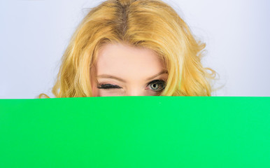 Winking woman with blank billboard. Woman hiding behind blank sign board. Advertising banner. Blonde girl peeking from behind blank sign. Woman hiding behind billboard. Message concept. Blank poster.