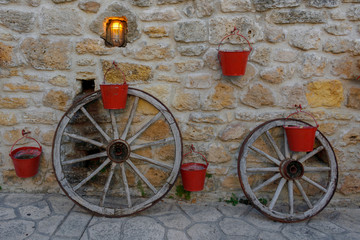 Stone wall decorated with red metal buckets and two bicycle frame wheels