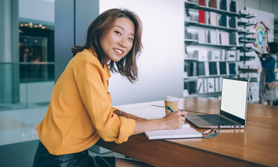 Female freelancer writing at desk in electronics store