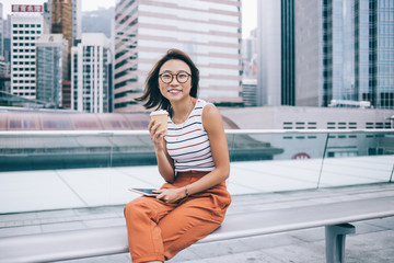 Cheerful Asian young woman having coffee sitting at street