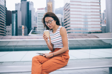 Asian woman enjoying coffee and using tablet on bench