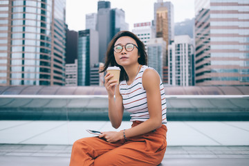 Fototapeta premium Dreamy young Asian woman with coffee on urban bench