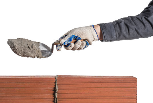 mano de obrero con camisa y guantes agarrando una pala con cemento sobre dos ladrillos naranjas unidos ocn cemento