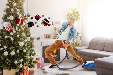 Young man cleaning with vacuum cleaner hardwood floor after New Year needles from Christmas tree in...