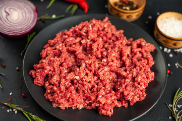 Fresh raw minced beef with herbs and spices on a black plate on a stone background