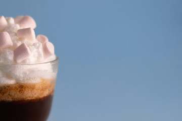 cup of coffee with whipped cream and marshmallows on a blue background