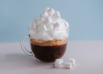 Cup of coffee with whipped cream and marshmallows on a pink tablecloth. Blue background, pastel colors.