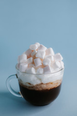 cup of coffee with whipped cream and marshmallows on a blue background