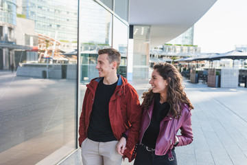 A trendy young couple walks around the city to shop, she is happy for what she sees in the shop window, love concept, Christmas shopping