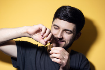 Portrait of young smiling man, opens a small gift, on yellow background.